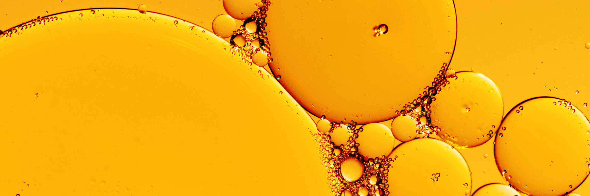Close-up of amber cold-pressed botanical oil forming round droplets against a golden ground