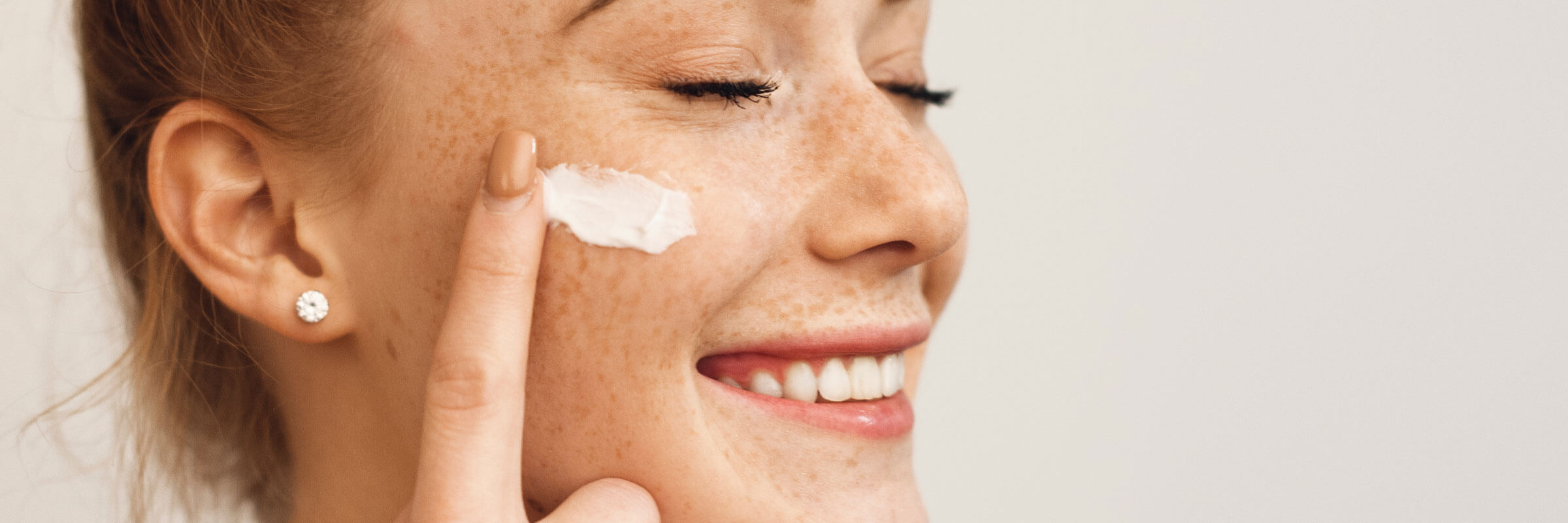 Woman with freckled skin smiling as she presses a peptide cream into her cheek