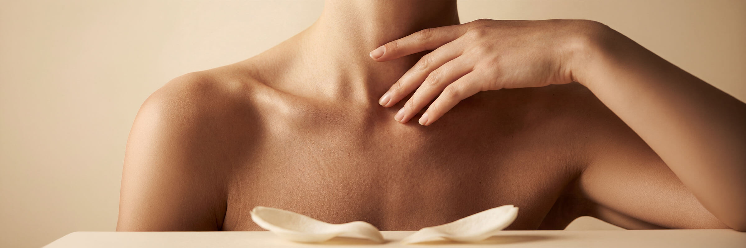 Close-up of a woman's shoulders and decolletage with her hands resting at her collarbone