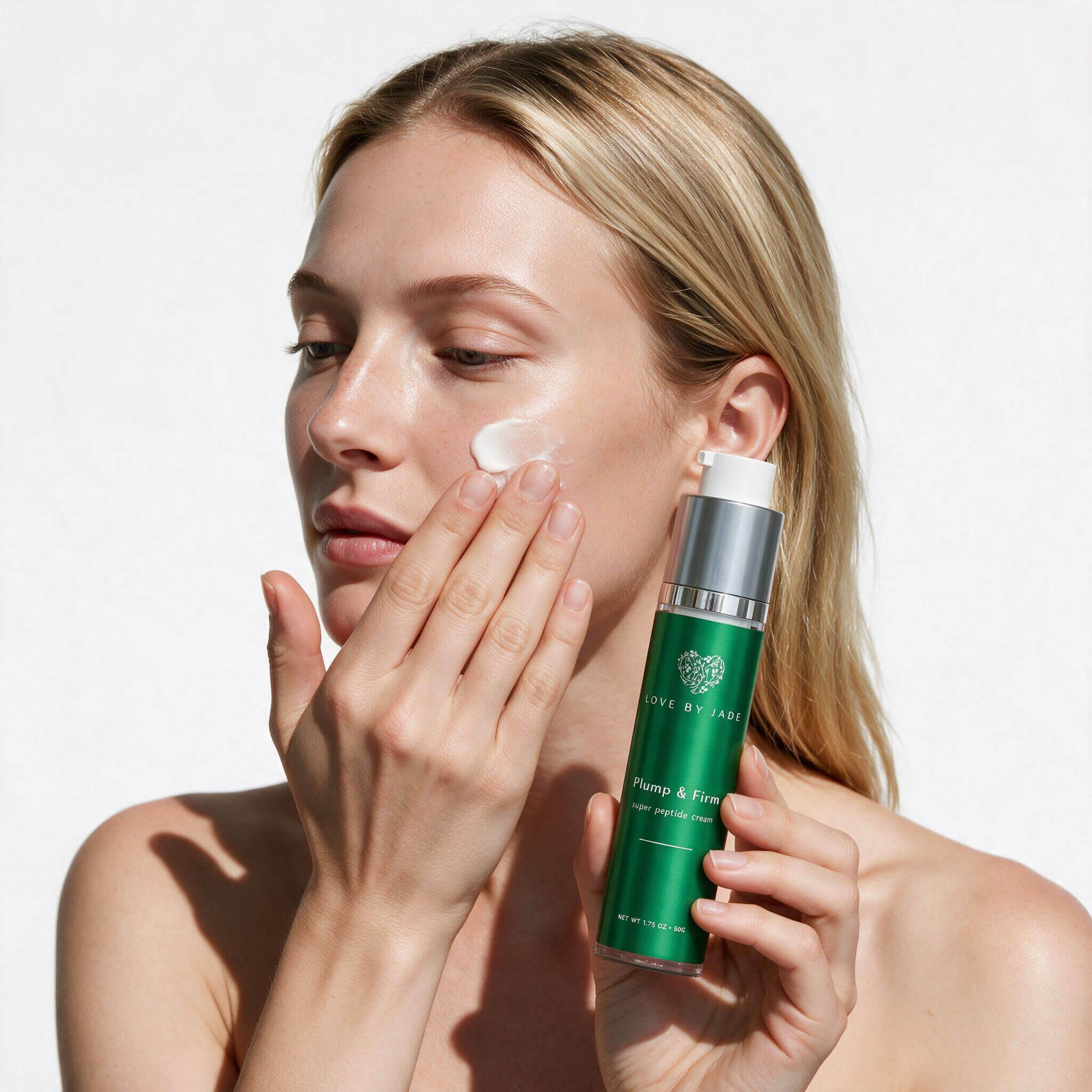 Woman smoothing Plump & Firm Super Peptide Cream onto her cheek with her fingertips, holding the 50g airless pump bottle.