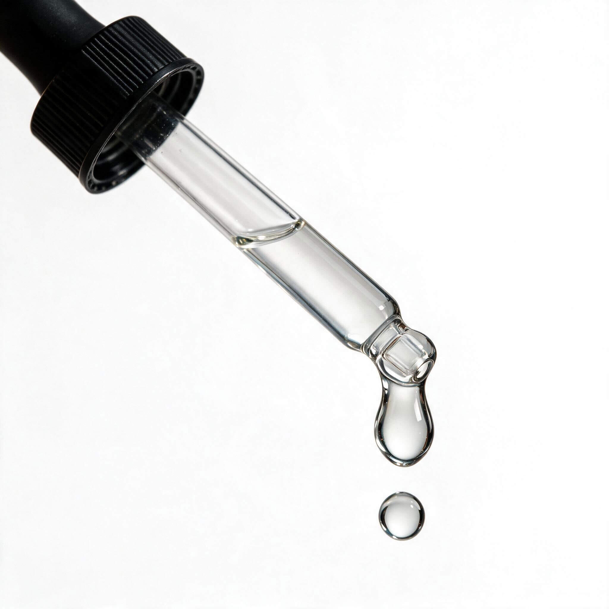 Macro of the Plump & Firm Serum glass dropper with a clear drop of serum falling from the tip.