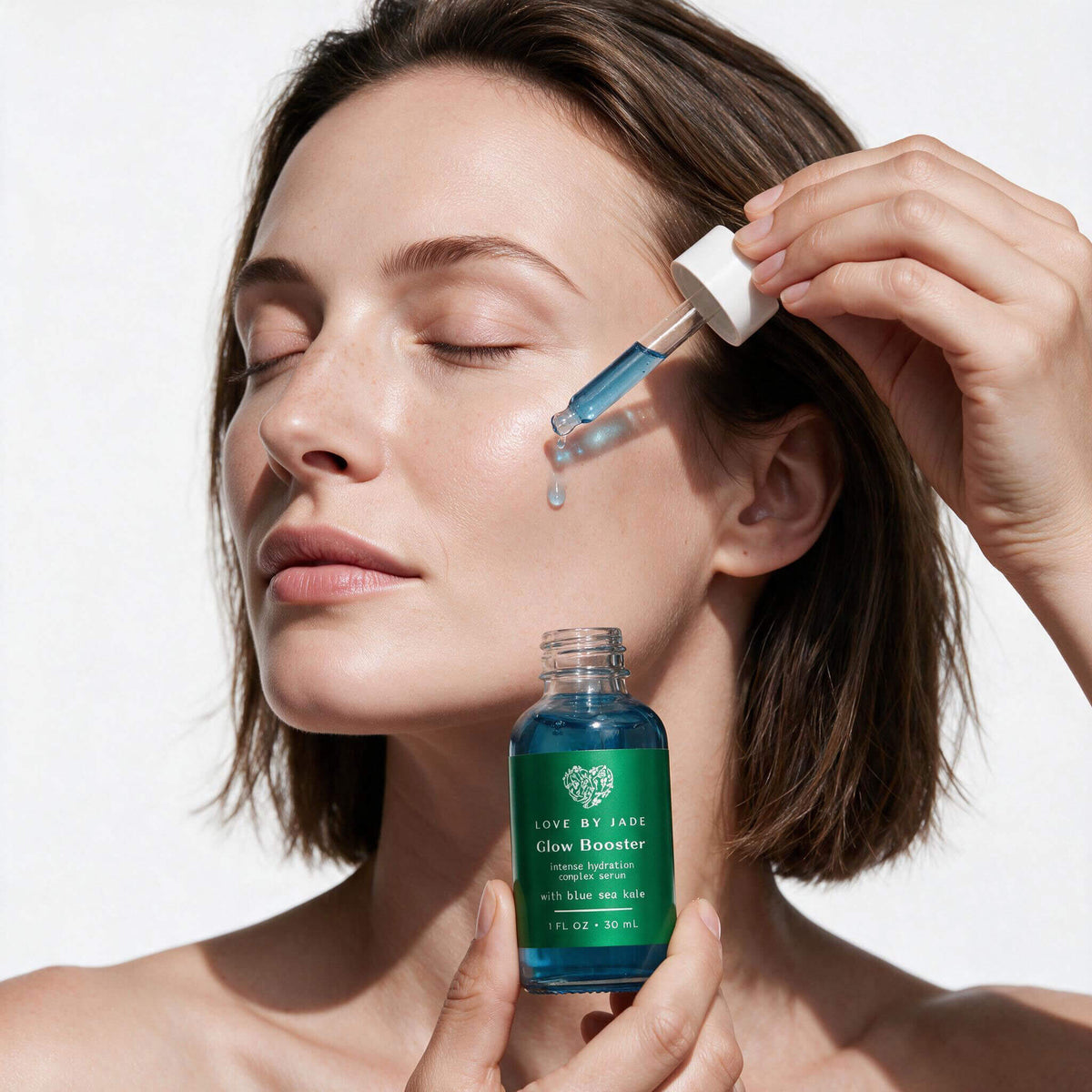 Woman pressing a drop of Glow Booster Intense Hydration Complex Serum into her cheek with the glass dropper, holding the 30ml bottle of blue serum.