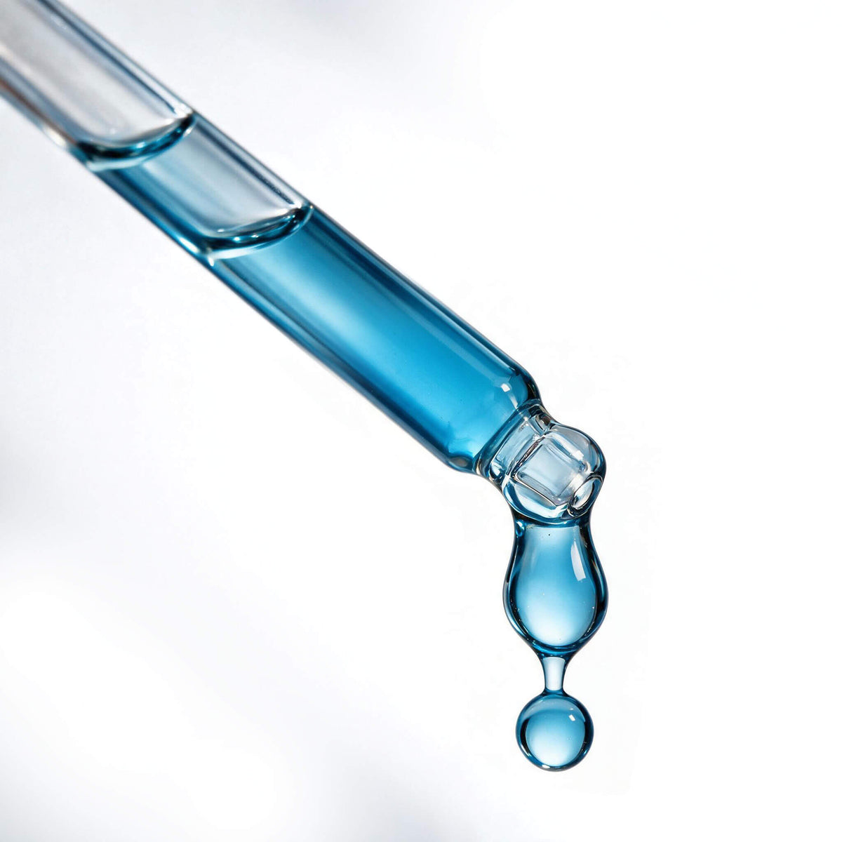 Macro of the Glow Booster glass dropper with a blue drop of serum falling from the tip.