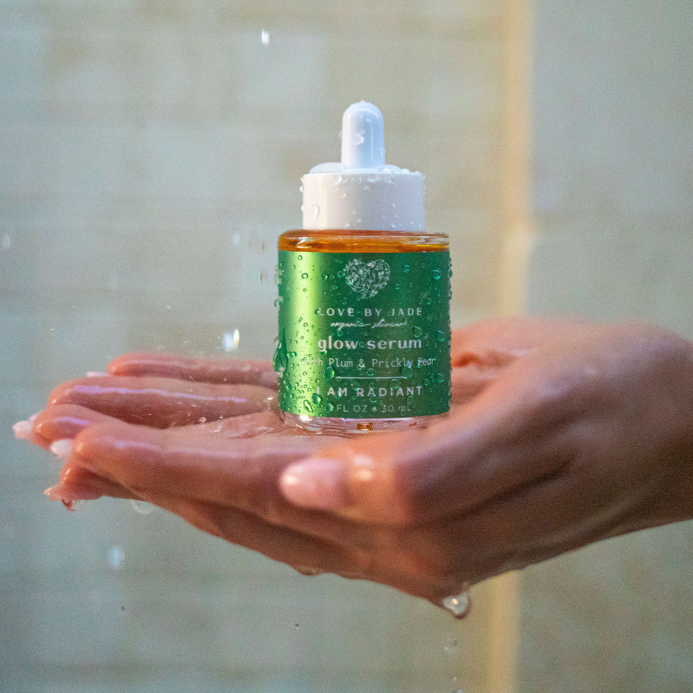 The Love by Jade Glow Face Serum bottle cupped in wet hands under running water